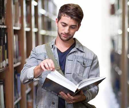 Young man reading a book in a library preparing for esl classes.